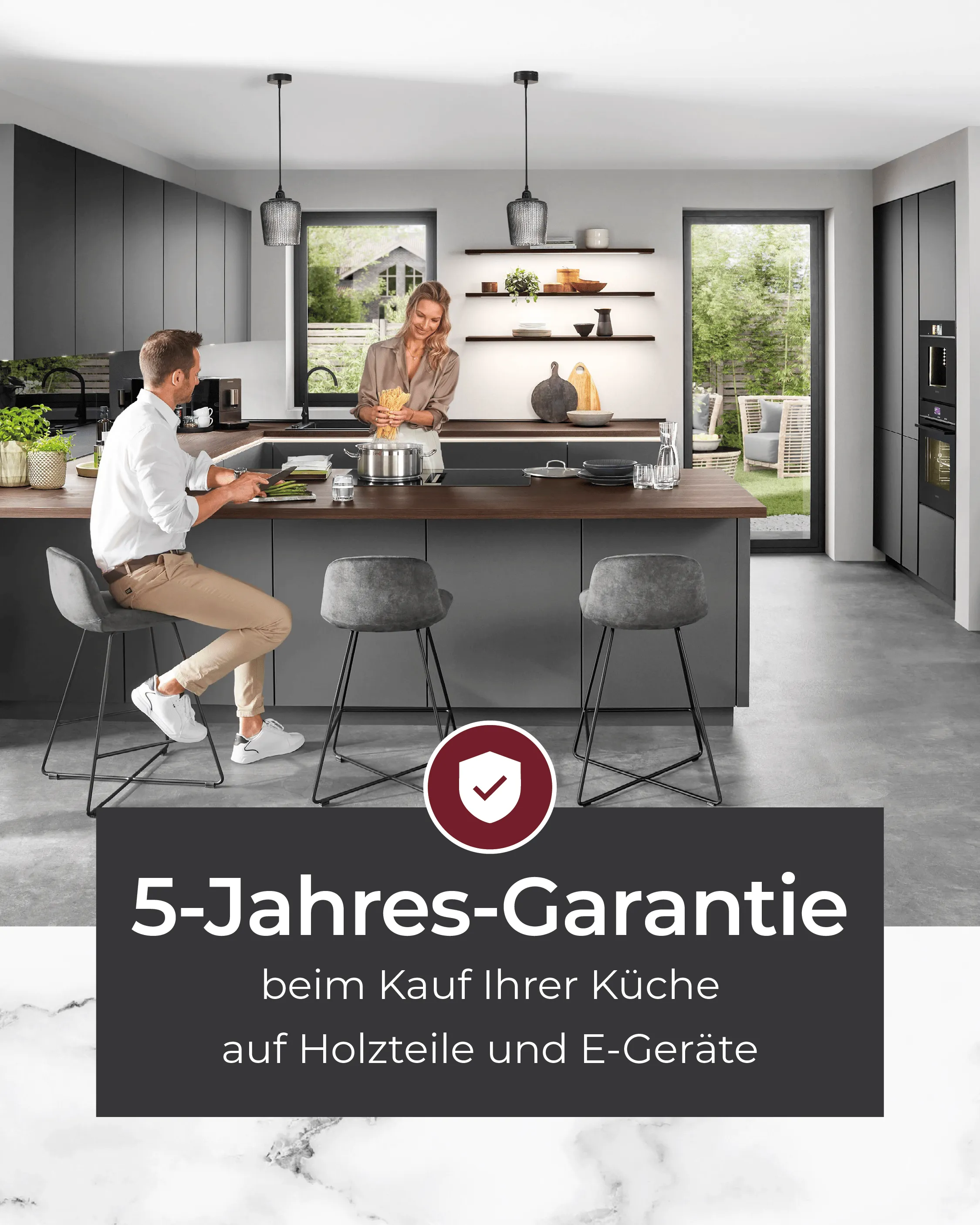 Designküche in dunklem Grau mit Kochinsel und Paar beim Kochen – Hinweis auf 5-Jahres-Garantie beim Küchenkauf auf Holzteile und Elektrogeräte
